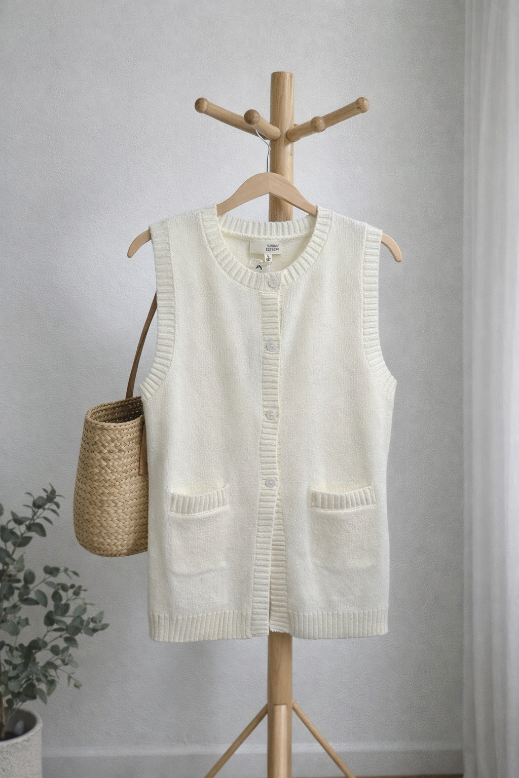 White knitted vest on a wooden hanger against a light gray wall.