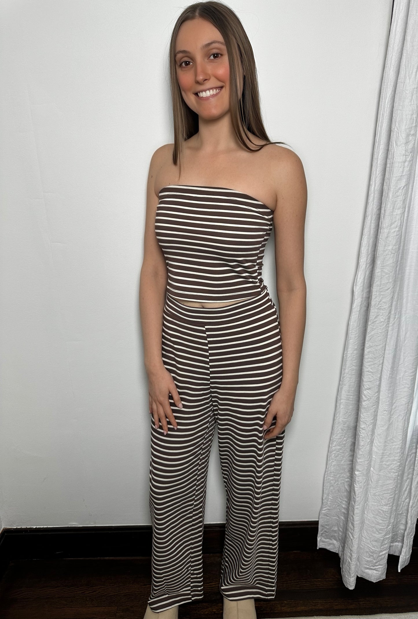 Woman wearing a black and white striped jumpsuit standing against a plain wall.