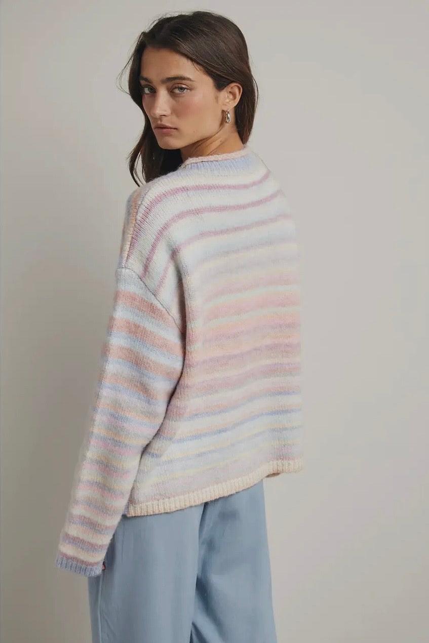 Woman wearing a striped pastel sweater and light blue pants against a plain background