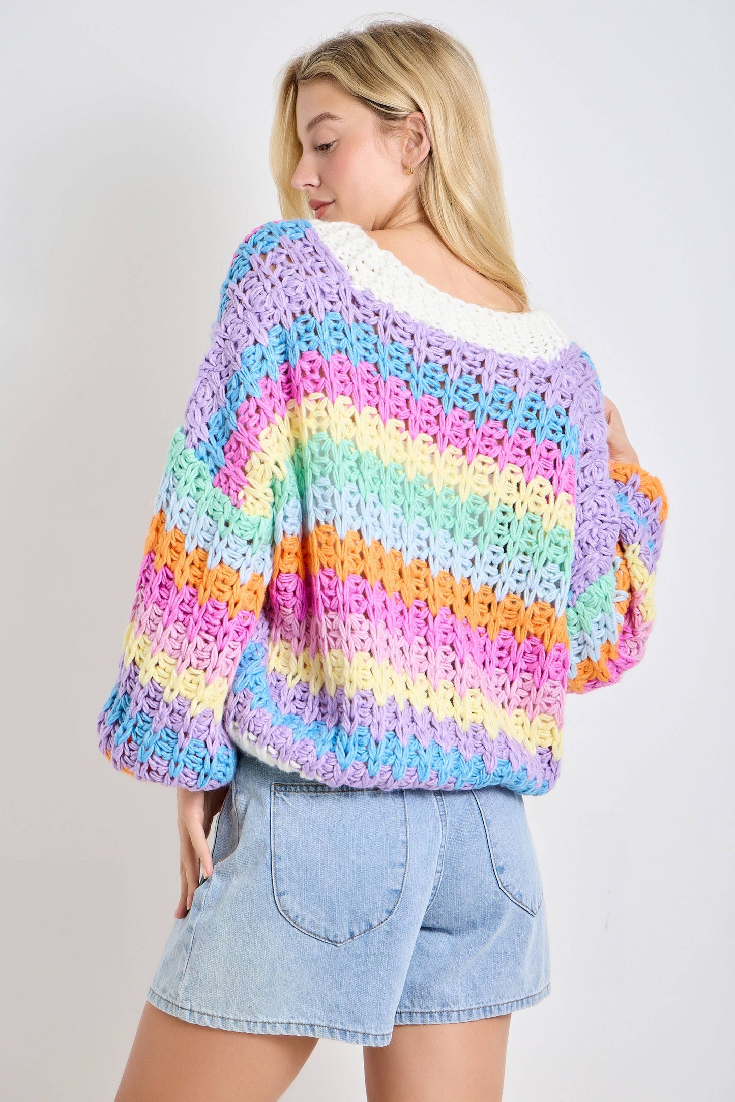 Woman wearing a colorful striped sweater and denim shorts on a plain background