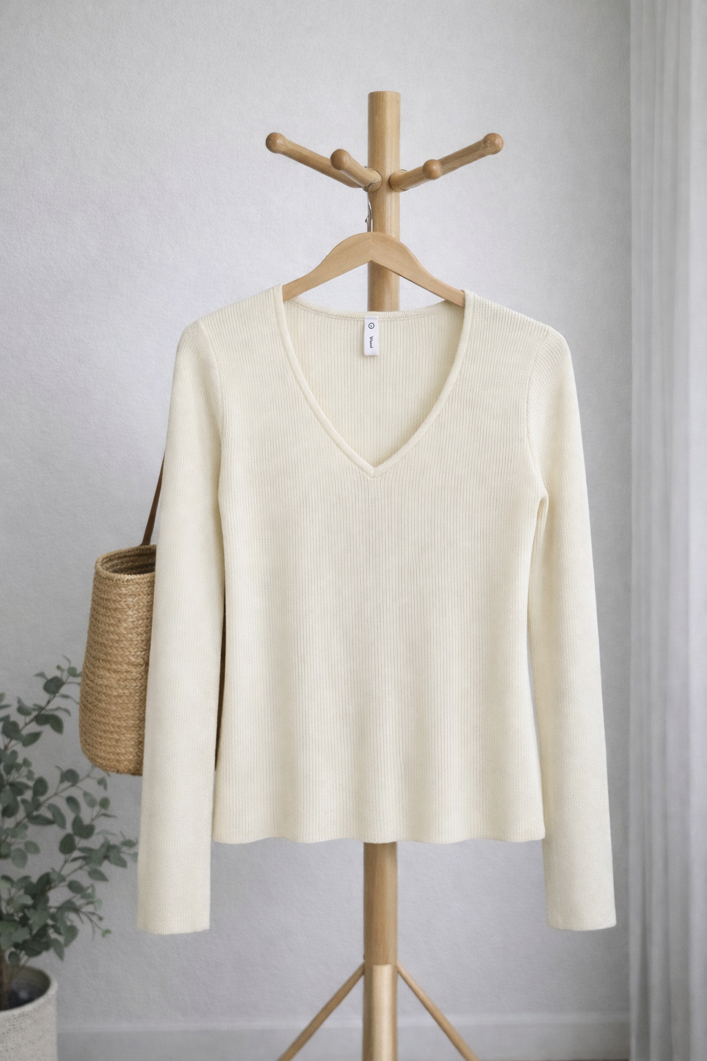 Cream-colored sweater on a wooden hanger against a gray wall.