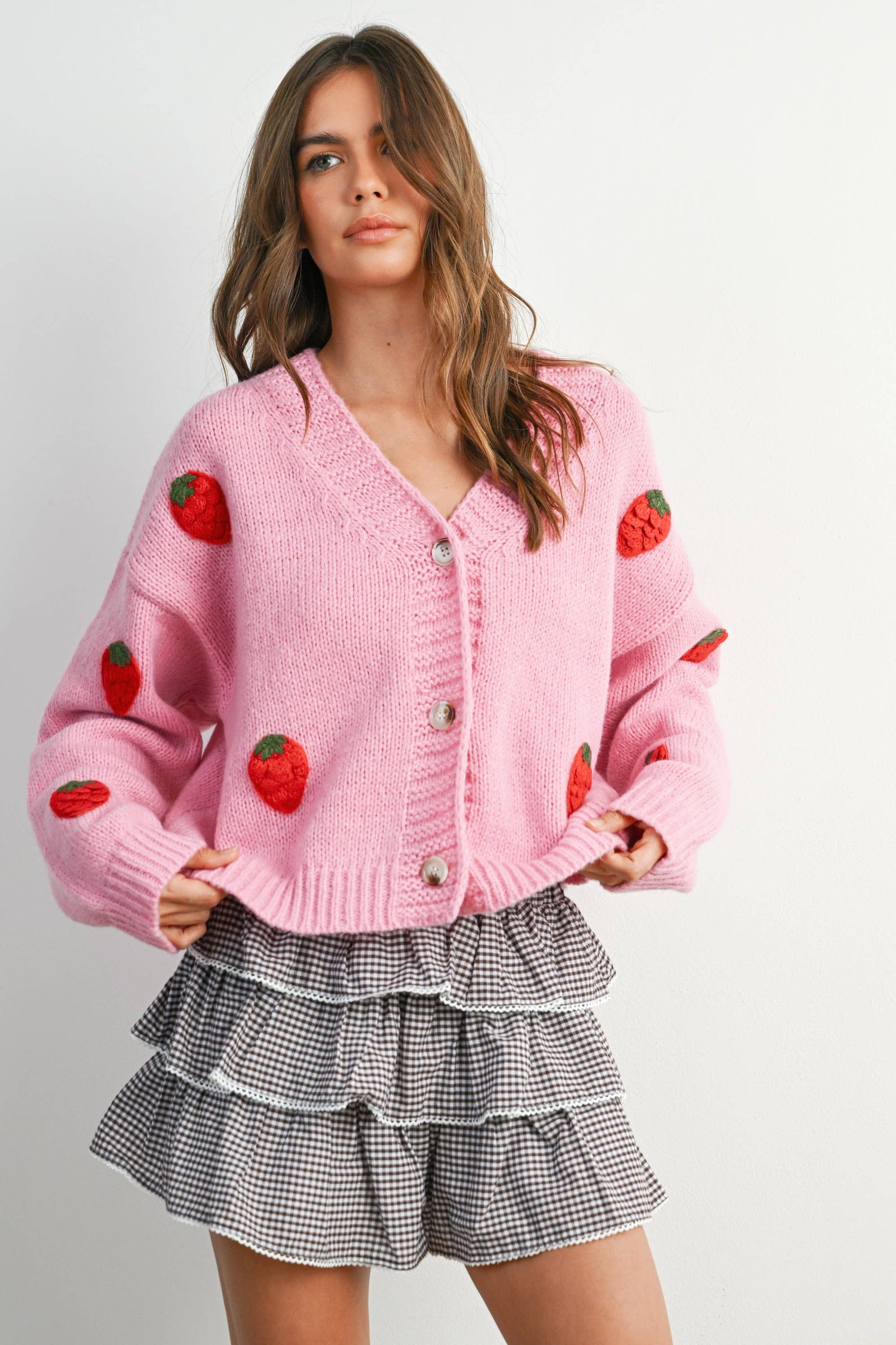 Woman wearing a pink cardigan with strawberry patterns on a plain background