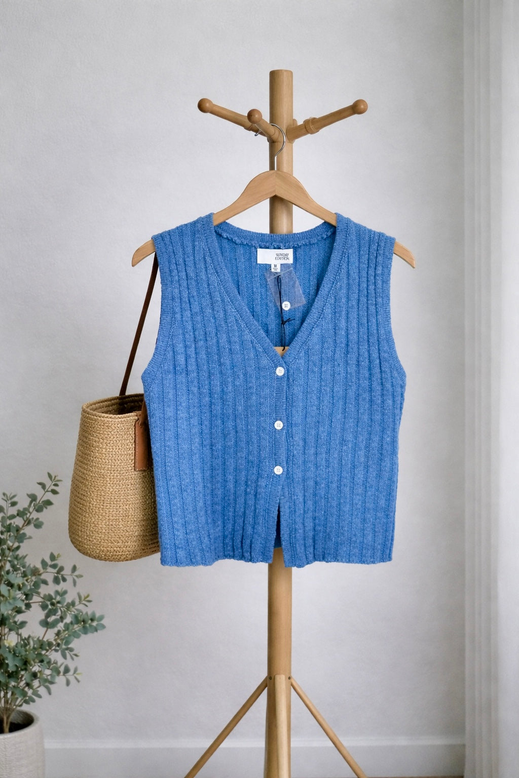 Blue knitted vest on a wooden hanger against a light gray wall.