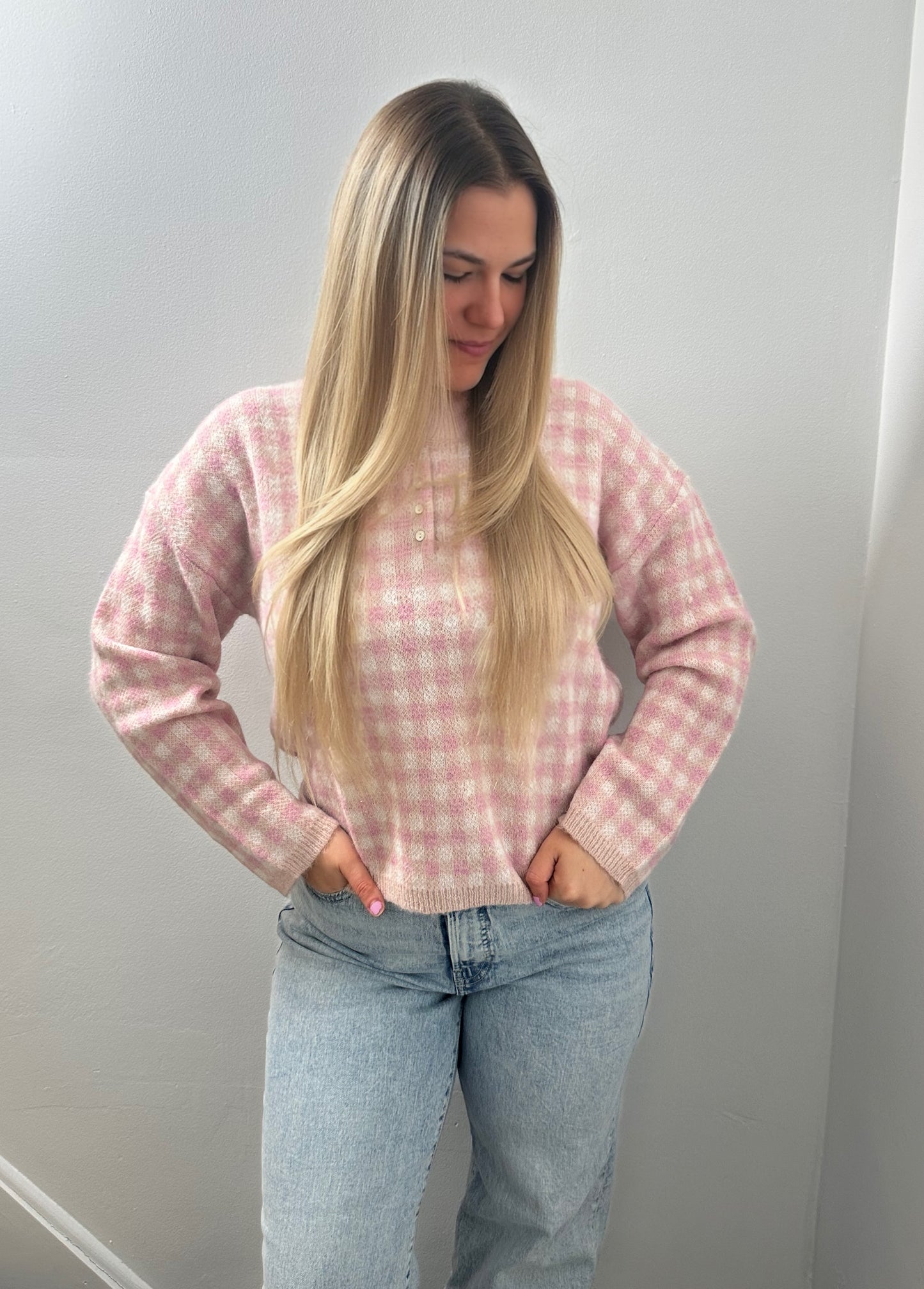 Woman wearing a pink checkered sweater and light blue jeans against a plain background