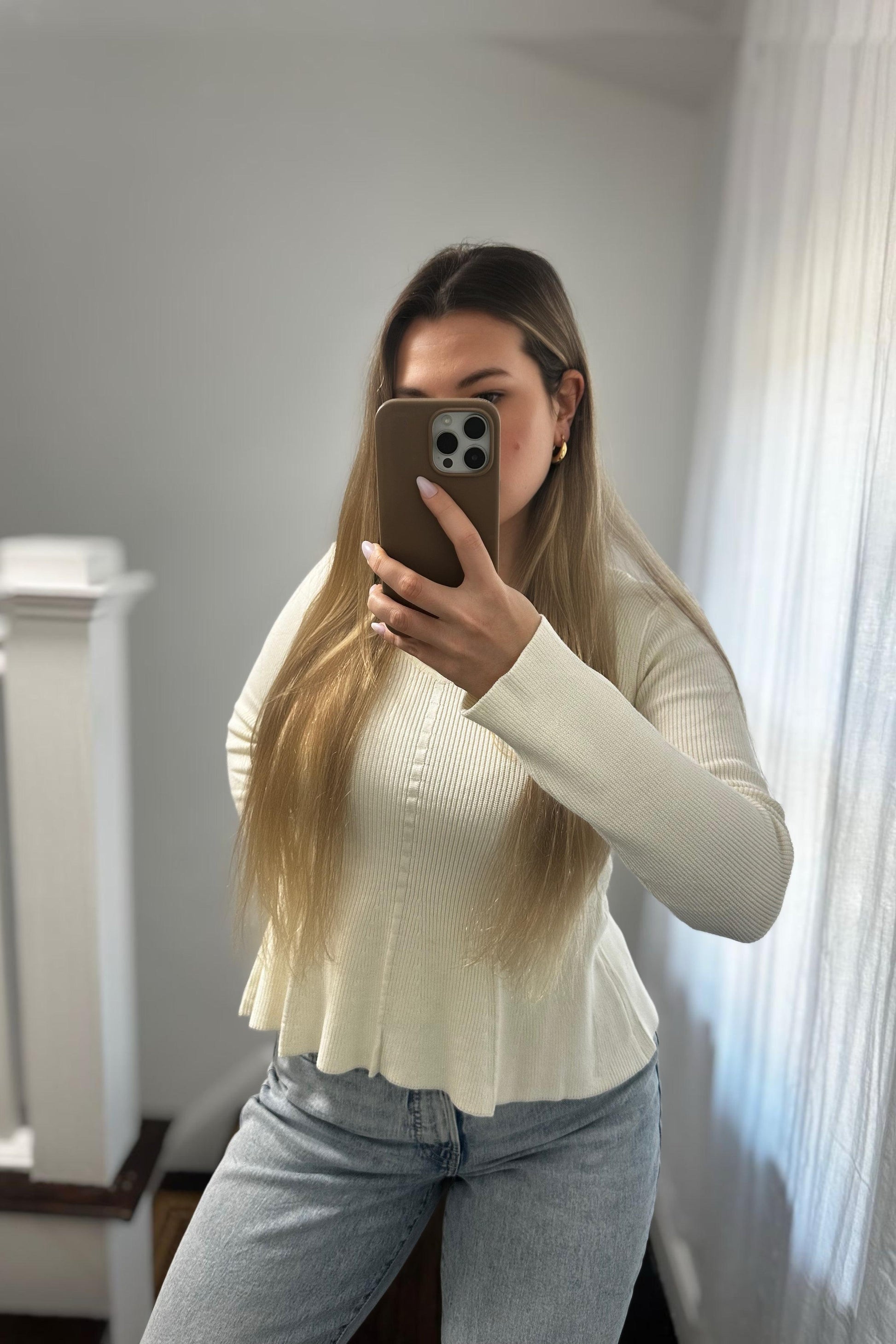 Person taking a mirror selfie wearing a white ribbed sweater and blue jeans.