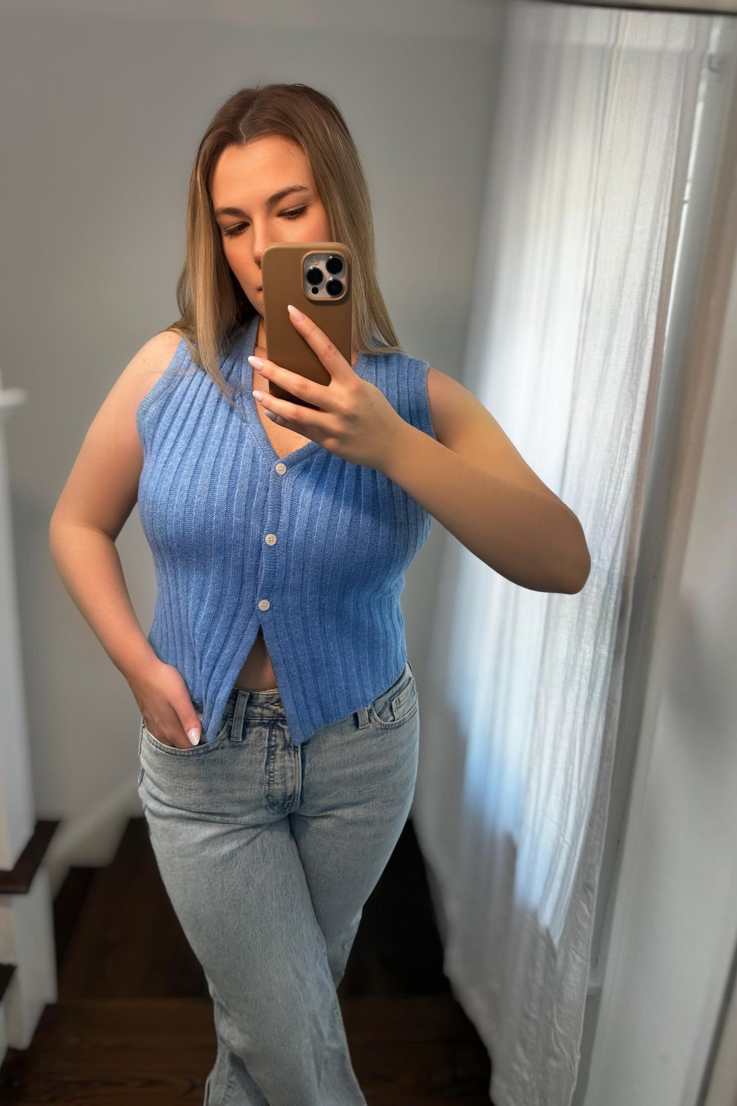 Woman taking a mirror selfie wearing a blue ribbed tank top and jeans.