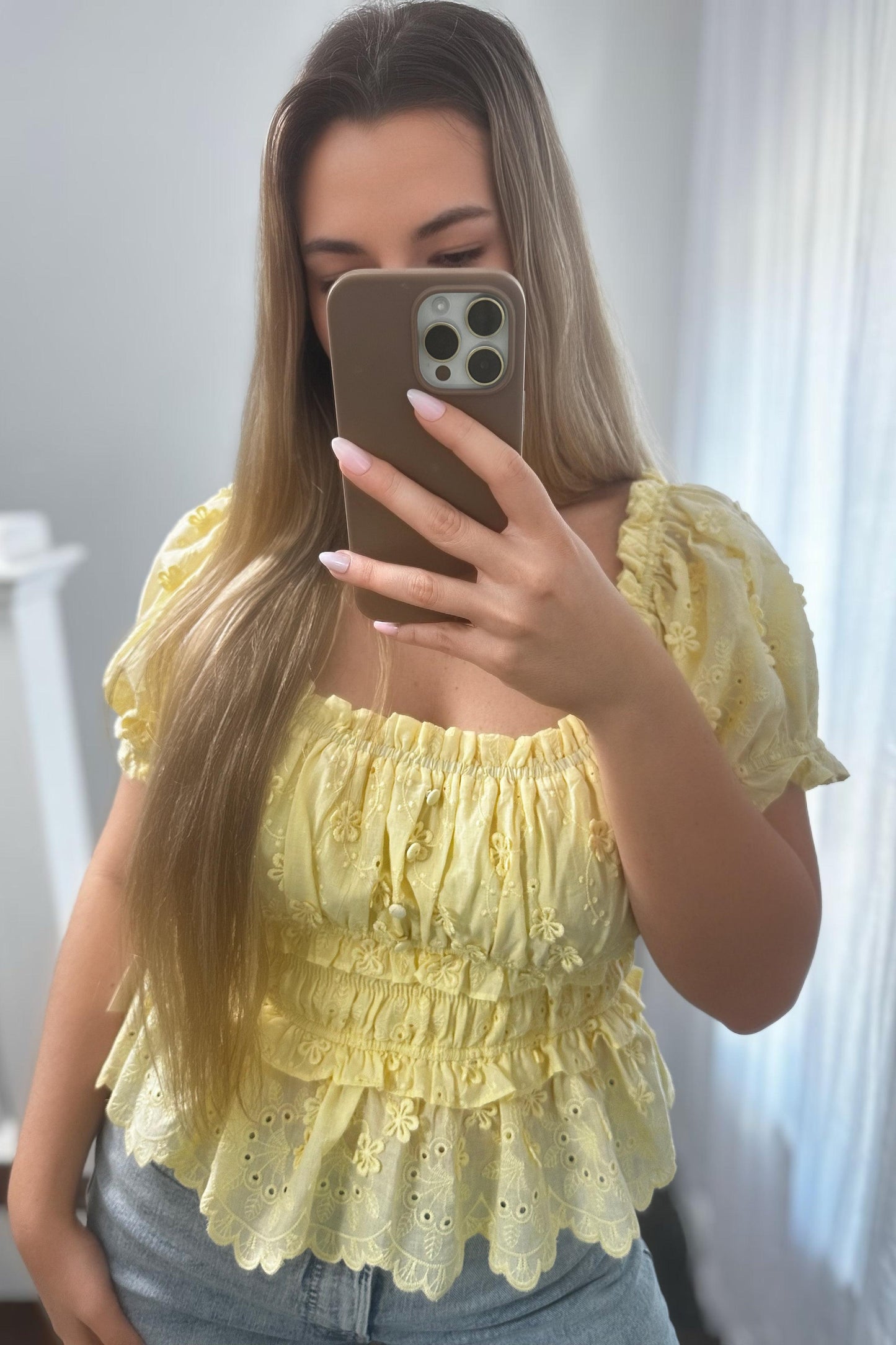Woman taking a mirror selfie wearing a yellow lace top.