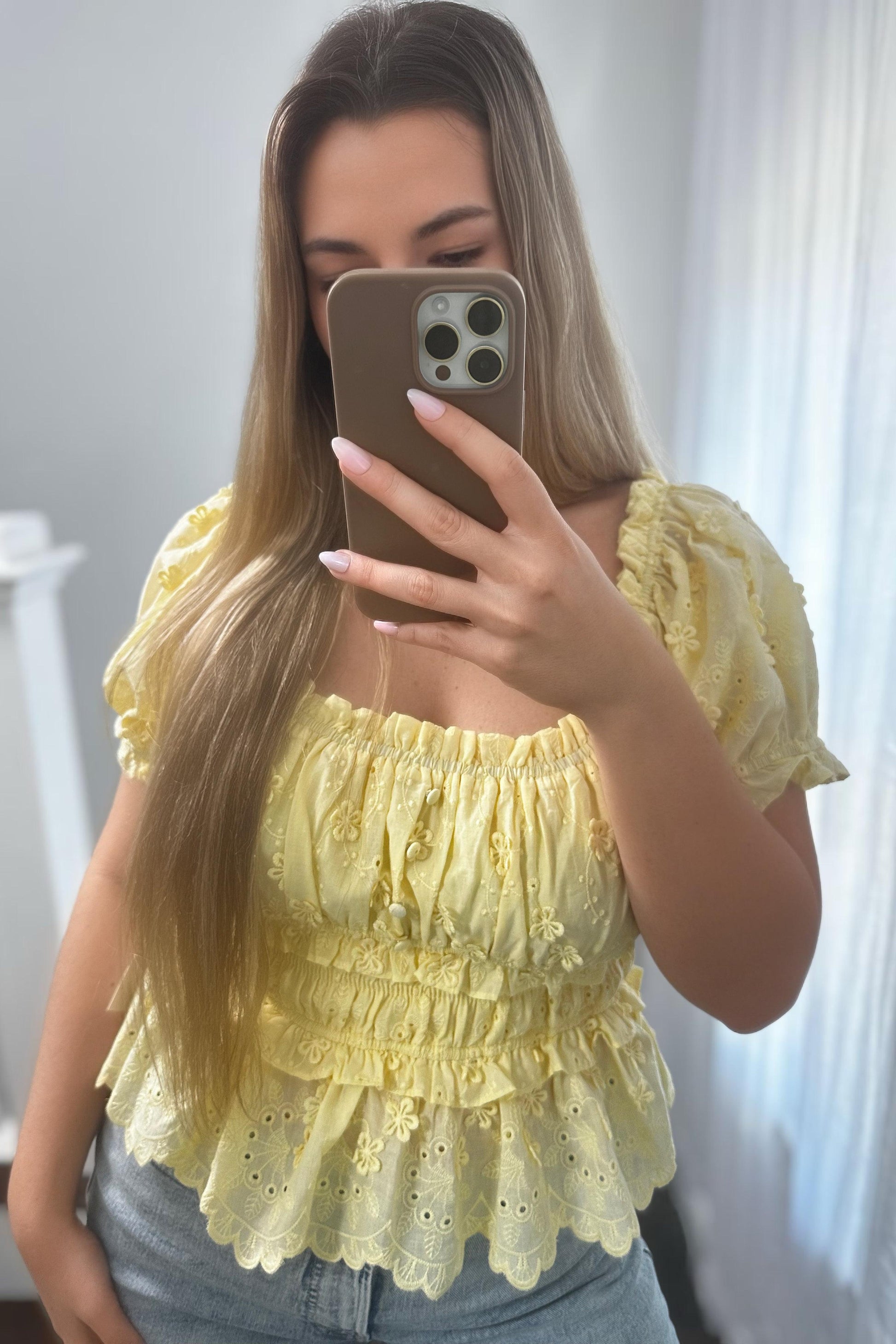 Woman taking a mirror selfie wearing a yellow lace top.