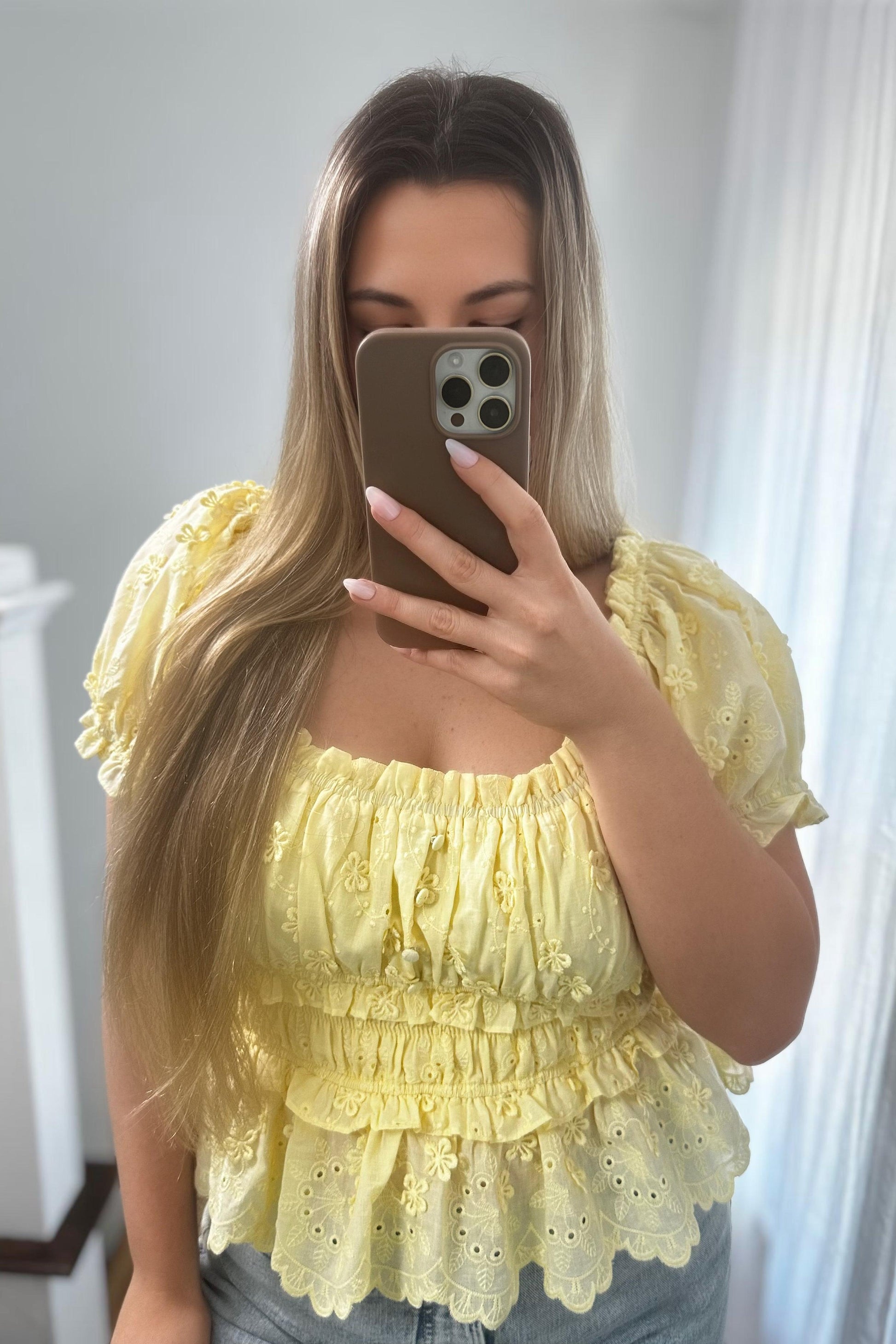 Woman taking a mirror selfie wearing a yellow lace top.