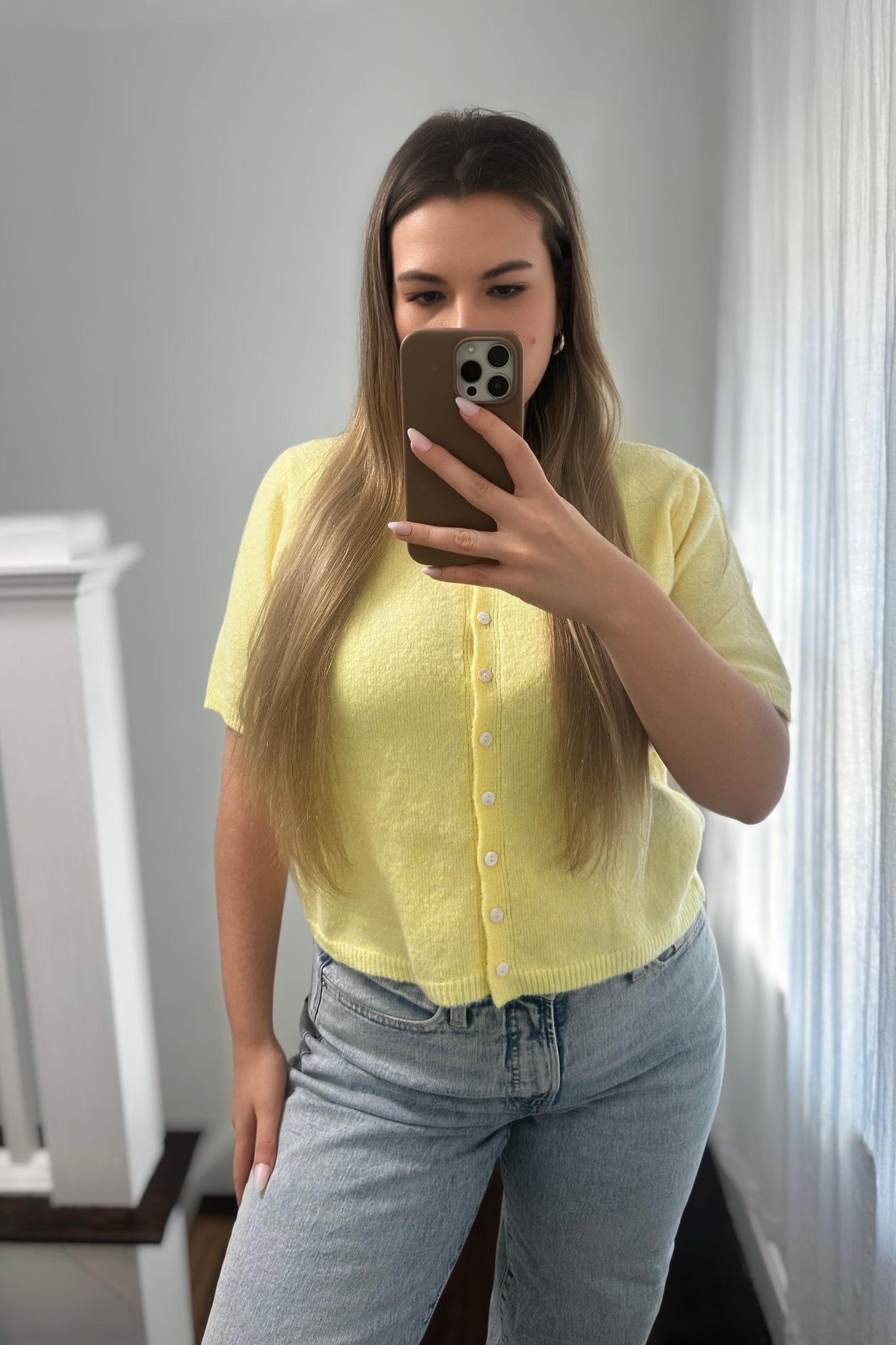 Person wearing a yellow seater cardigan and blue jeans taking a mirror selfie.