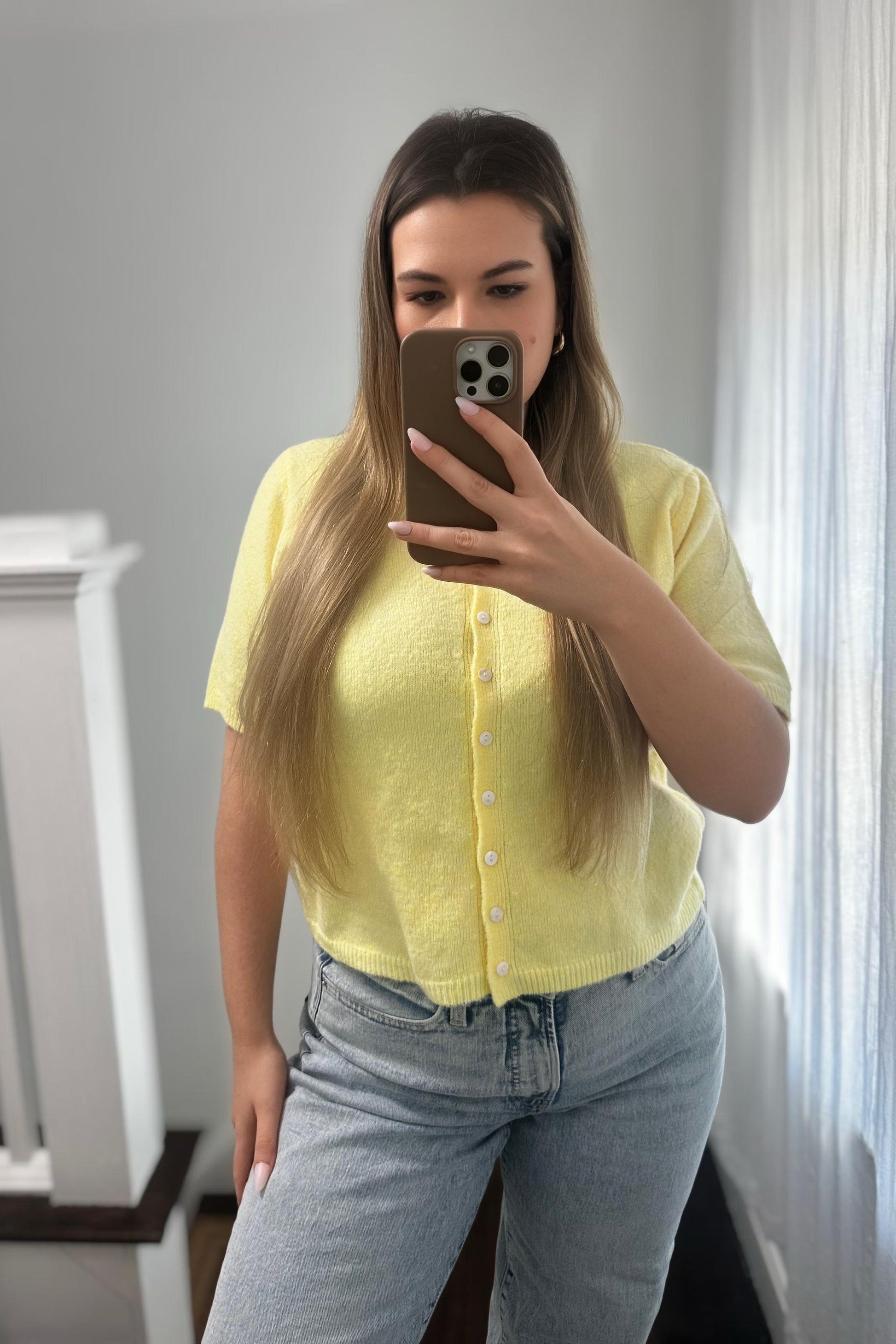 Person wearing a yellow seater cardigan and blue jeans taking a mirror selfie.