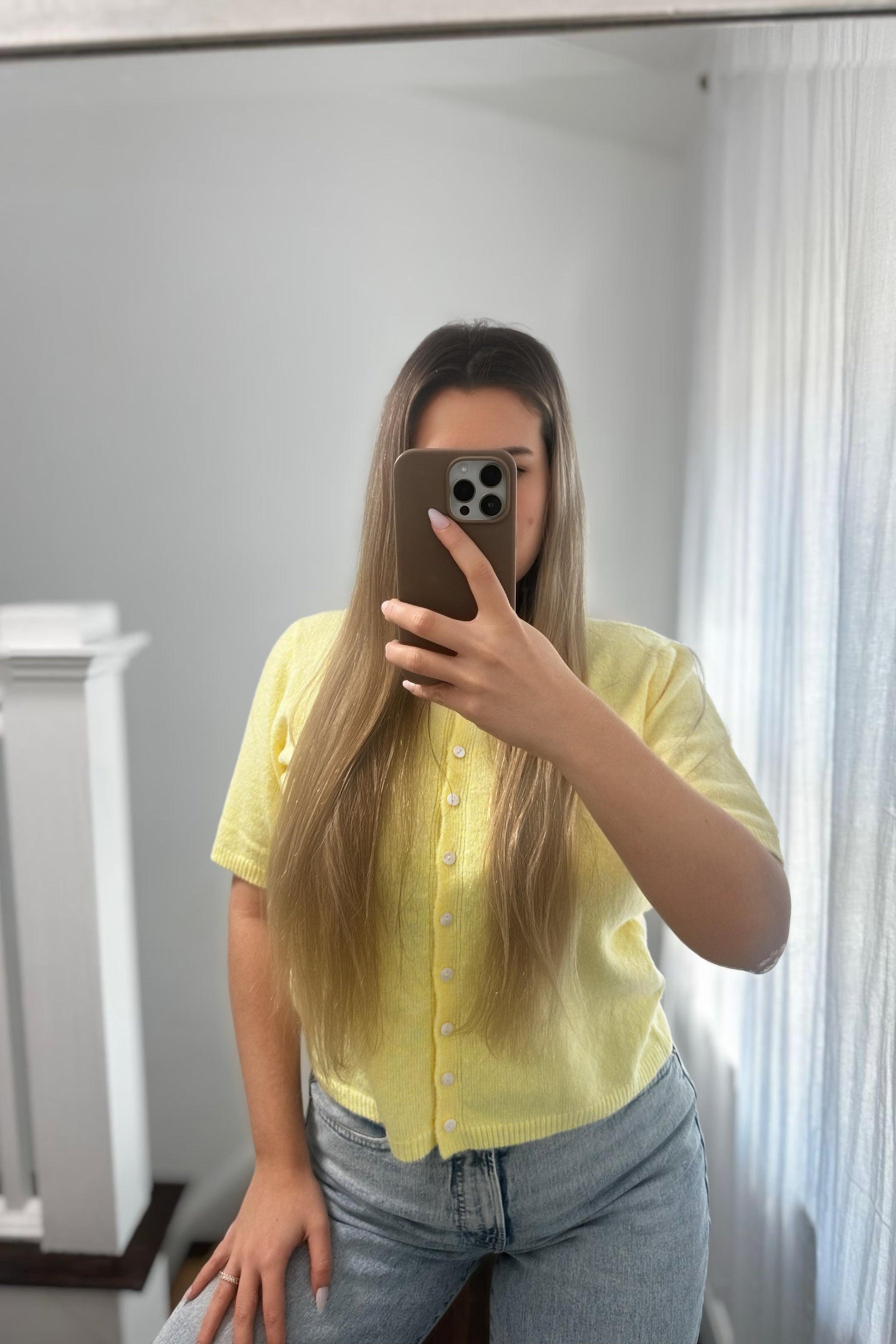Person wearing a yellow seater cardigan and blue jeans taking a mirror selfie.