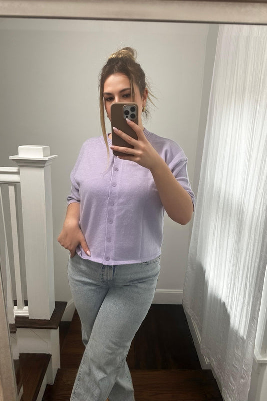 Person taking a mirror selfie wearing a light purple shirt and light blue jeans in a home setting.