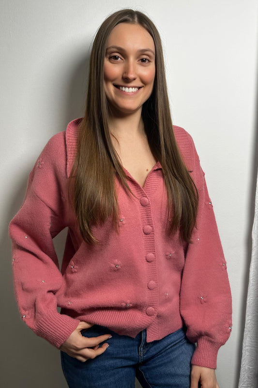 Woman wearing a pink cardigan with decorative buttons against a plain background