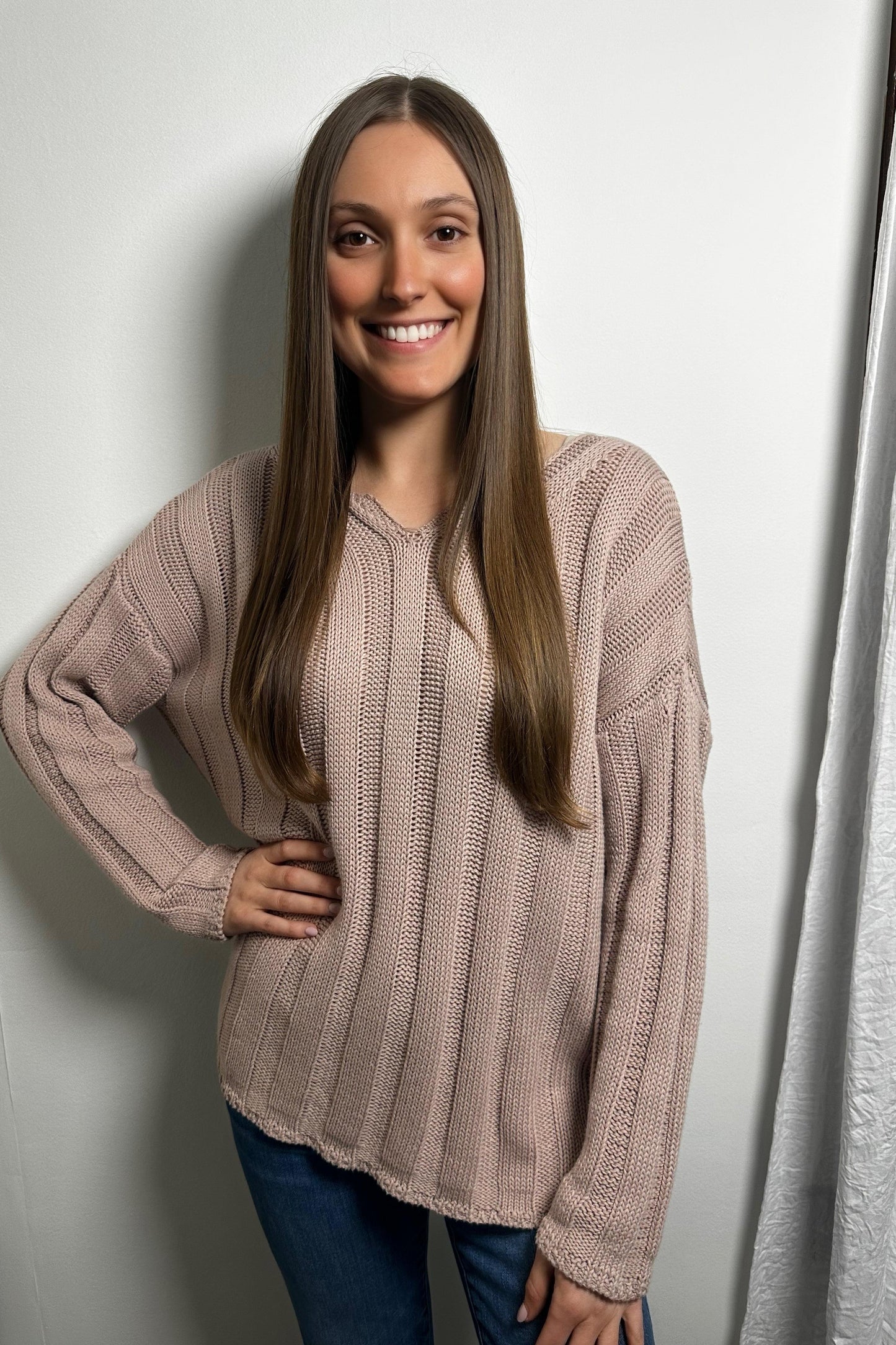 Woman wearing a beige sweater against a white wall