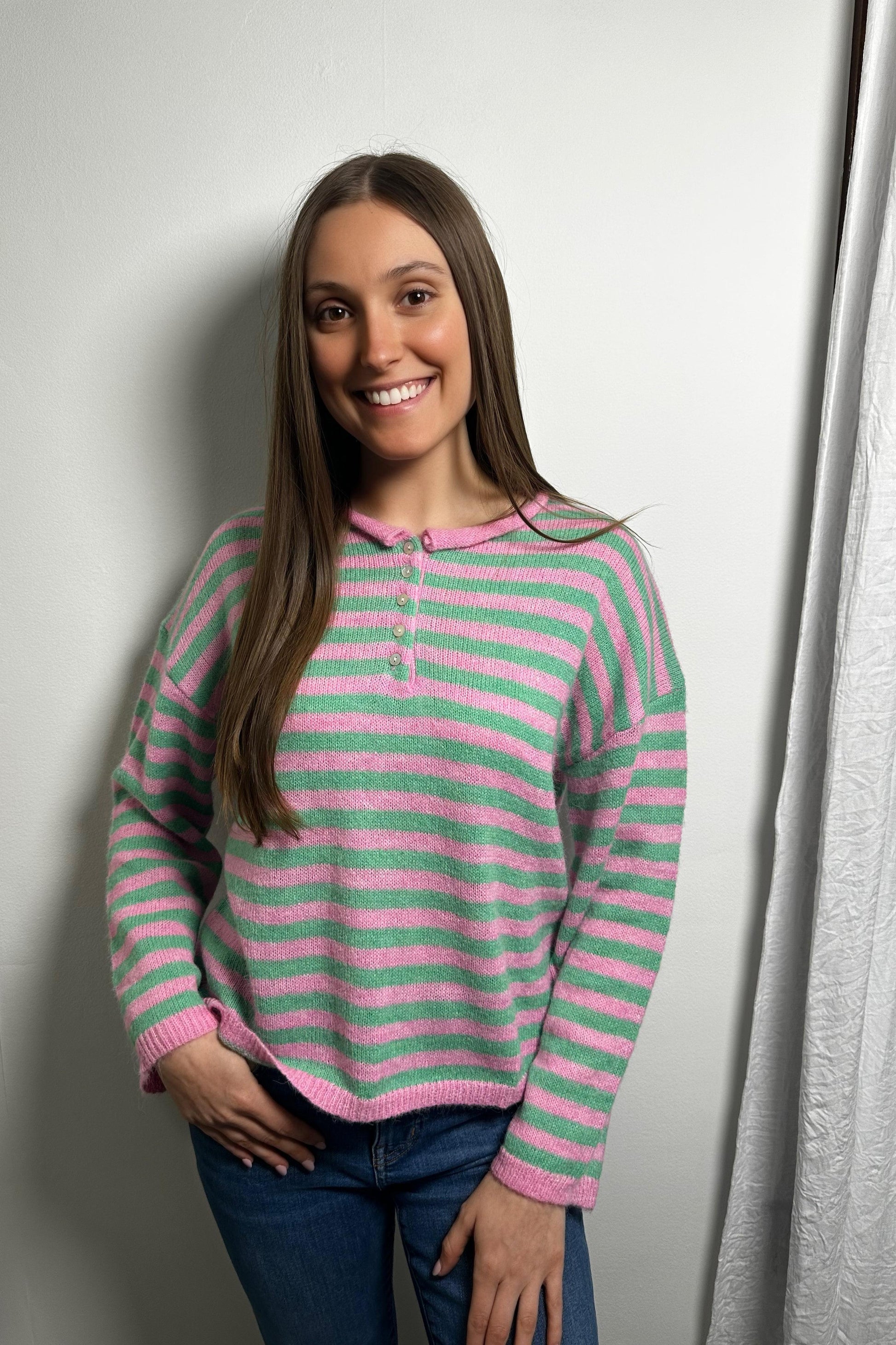 Woman wearing a pink and green striped sweater against a white wall.