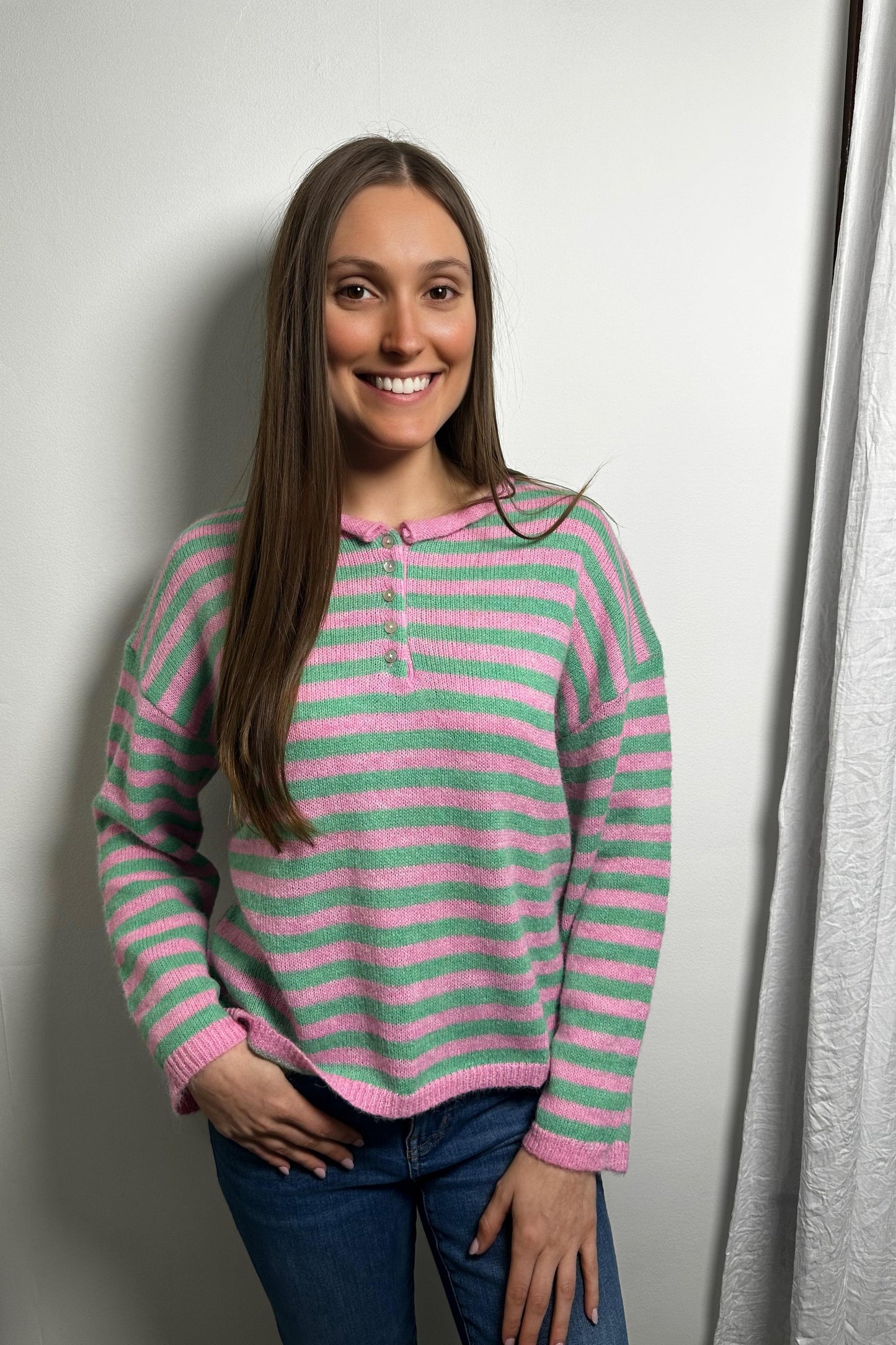 Woman wearing a pink and green striped sweater against a white wall.