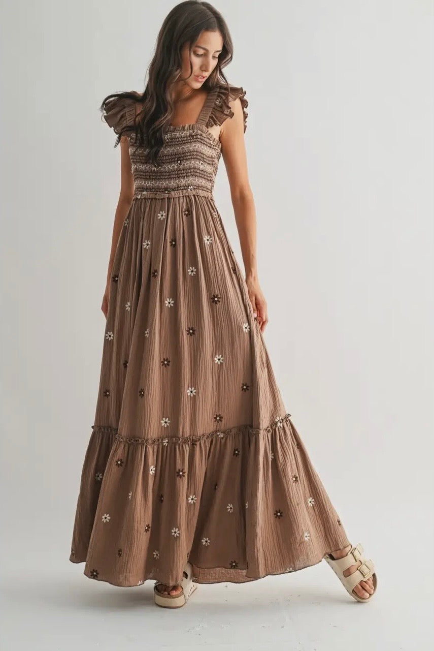 Woman wearing a long brown dress with floral patterns on a plain background