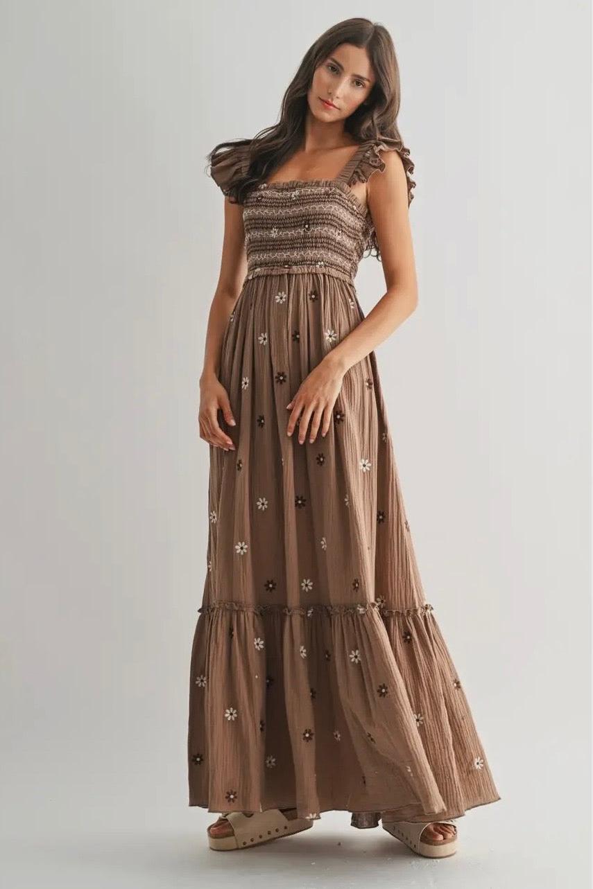 Woman wearing a long brown dress with floral patterns on a plain background