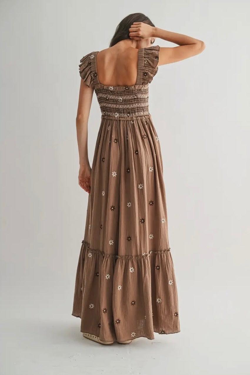 Woman wearing a long brown dress with floral patterns on a plain background