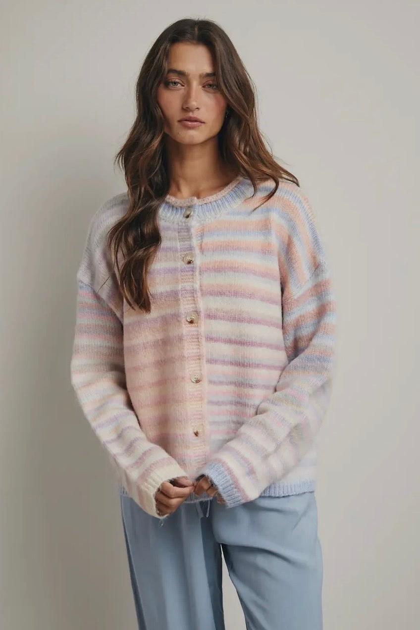 Woman wearing a striped pastel sweater and light blue pants against a plain background