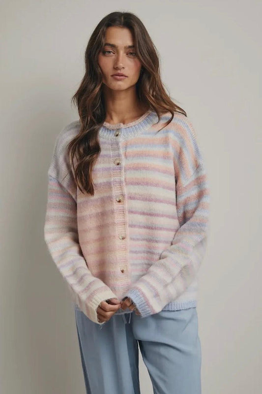 Woman wearing a striped pastel sweater and light blue pants against a plain background