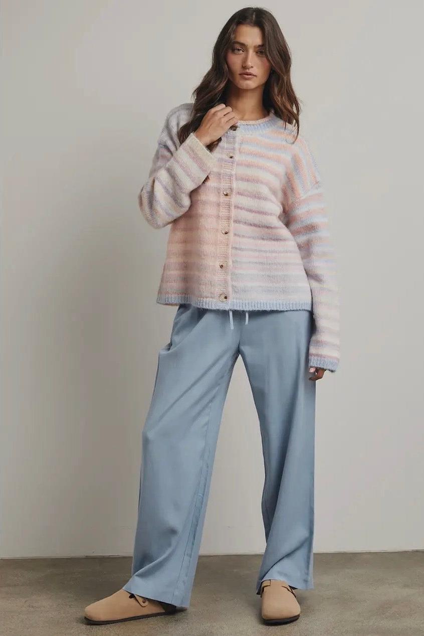 Woman wearing a striped pastel sweater and light blue pants against a plain background