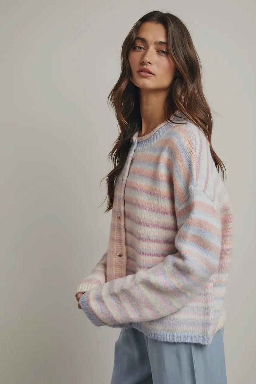 Woman wearing a striped pastel sweater and light blue pants against a plain background