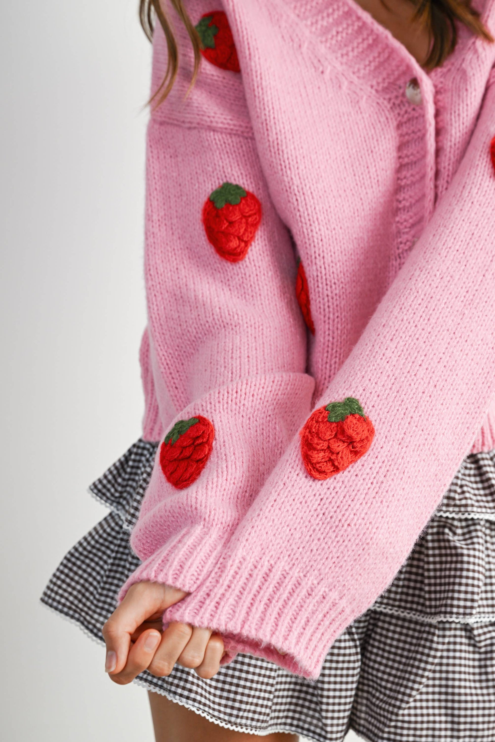 Pink knitted cardigan with strawberry patterns worn by a person on a plain background