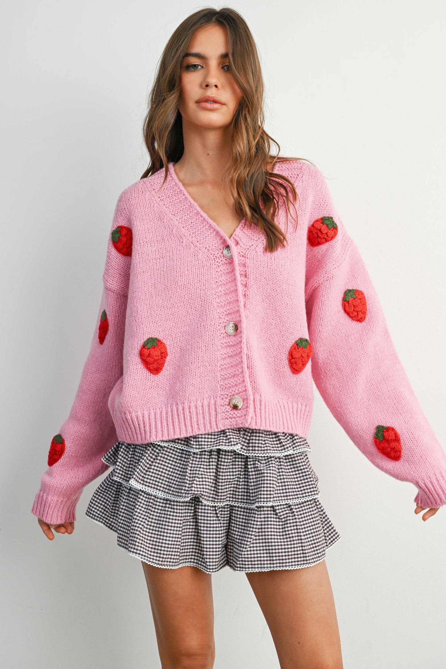 Woman wearing a pink cardigan with strawberry patterns on a plain background