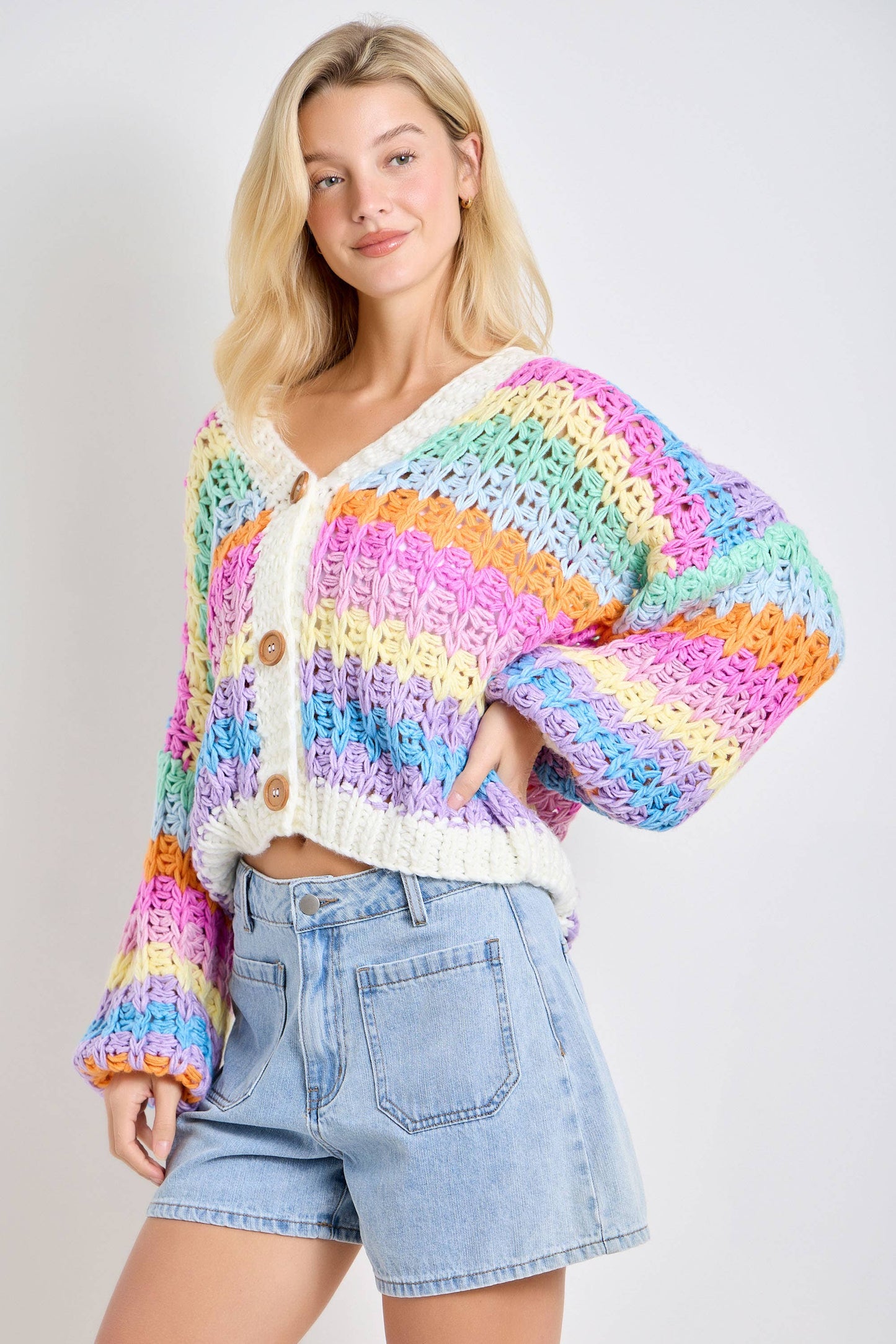 Woman wearing a colorful striped sweater and denim shorts on a plain background