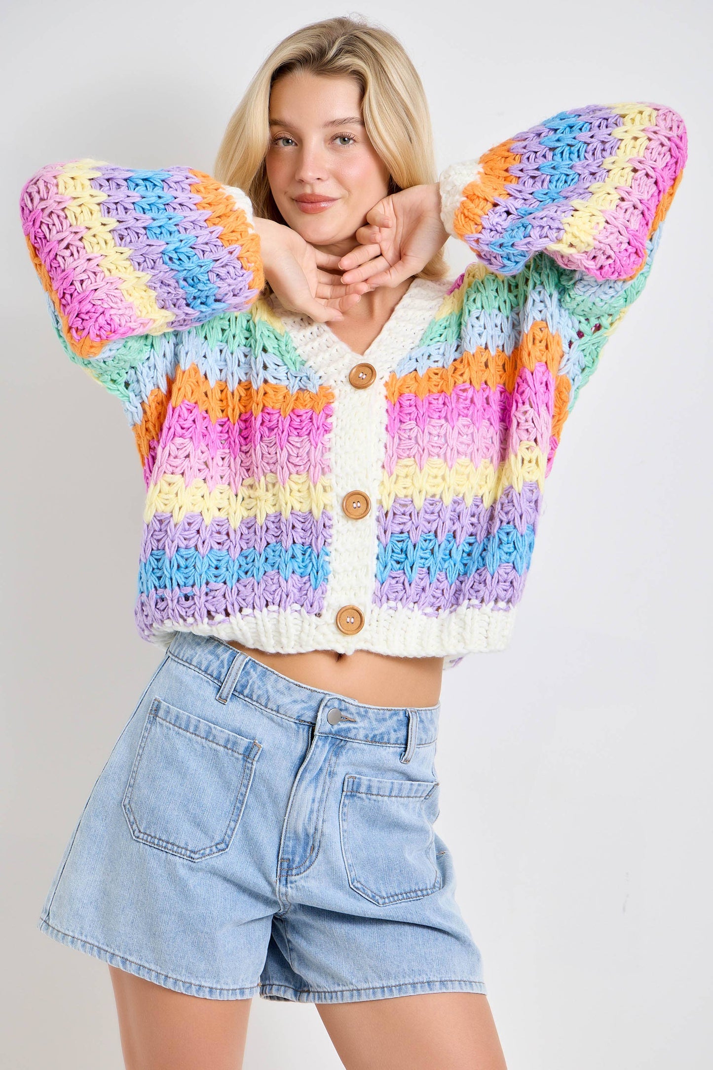 Woman wearing a colorful striped sweater and denim shorts on a plain background