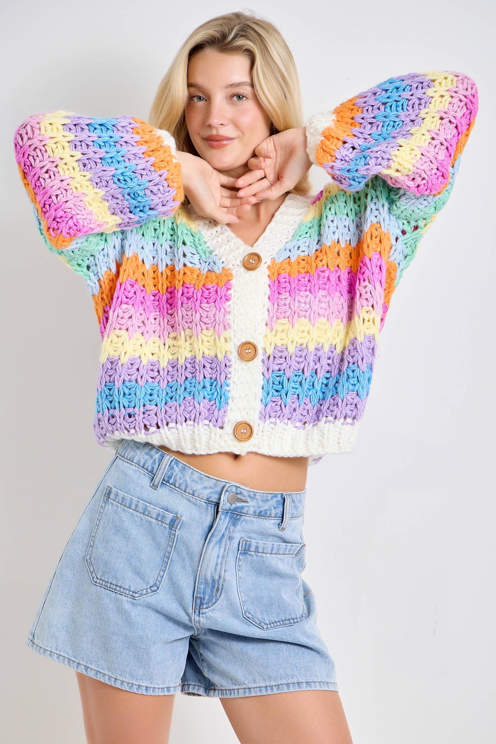 Woman wearing a colorful striped sweater and denim shorts on a plain background
